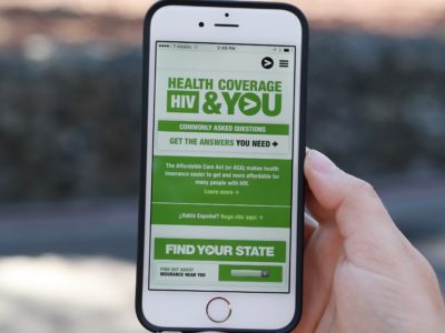 Hand holding smartphone displaying Greater Than HIV Health Coverage, HIV and You campaign website